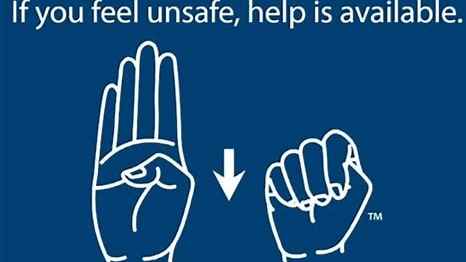 Face your palm toward the person you want to alert.  Tuck your thumb into your palm.  Fold your fingers down over the thumb, trapping it in your fist.