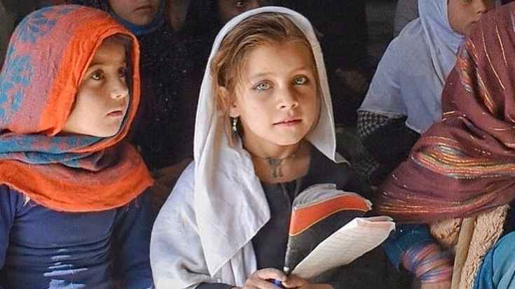 “A young girl in a headscarf holding books, looking forward with determination.”