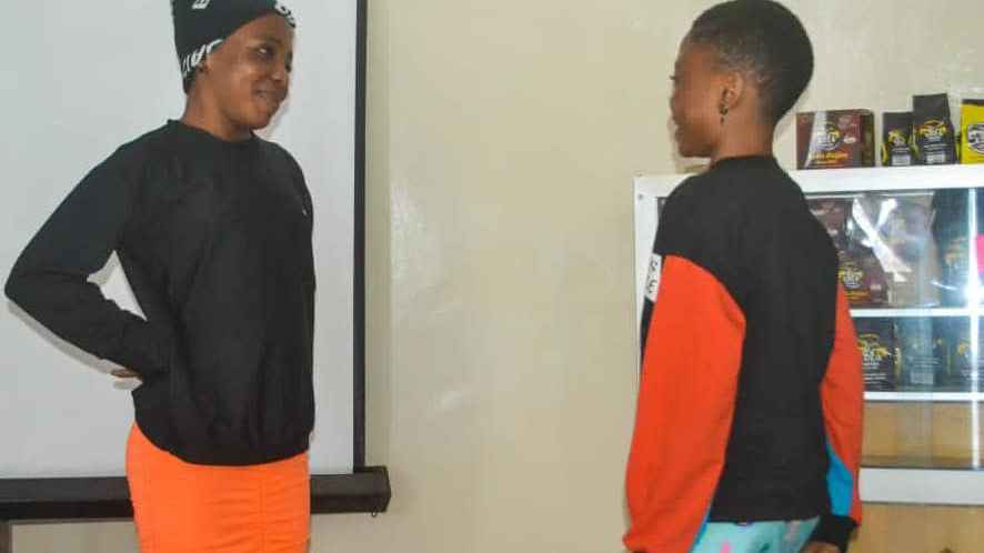 Two adolescent girls standing face to face with each other, one wearing a black shirt over an orange pants and the other wearing a black and orange shirt over  a sky blue flourish pants.
