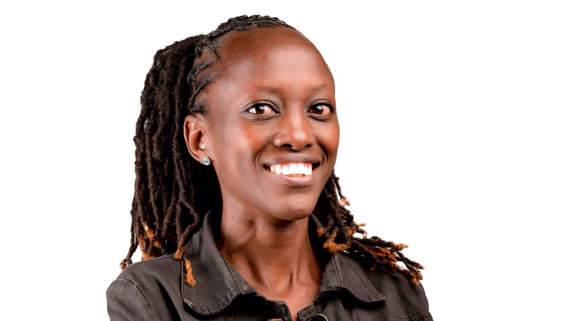 Kurui, a woman from Kenya, smiles. She has long, dark braided hair, a black collared top, and earrings. 