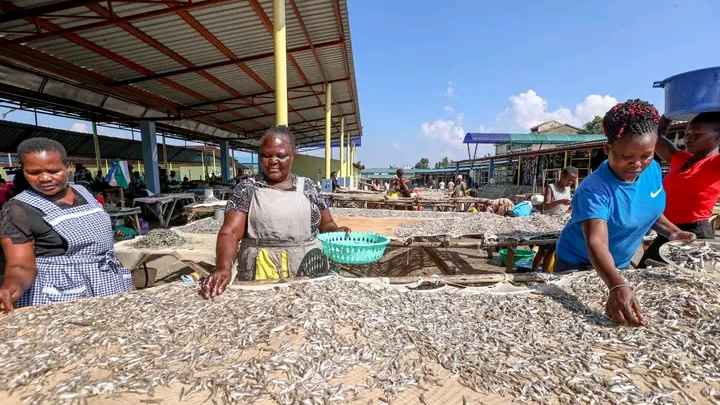 The image describes hard work by women along the lake despite the challenges 