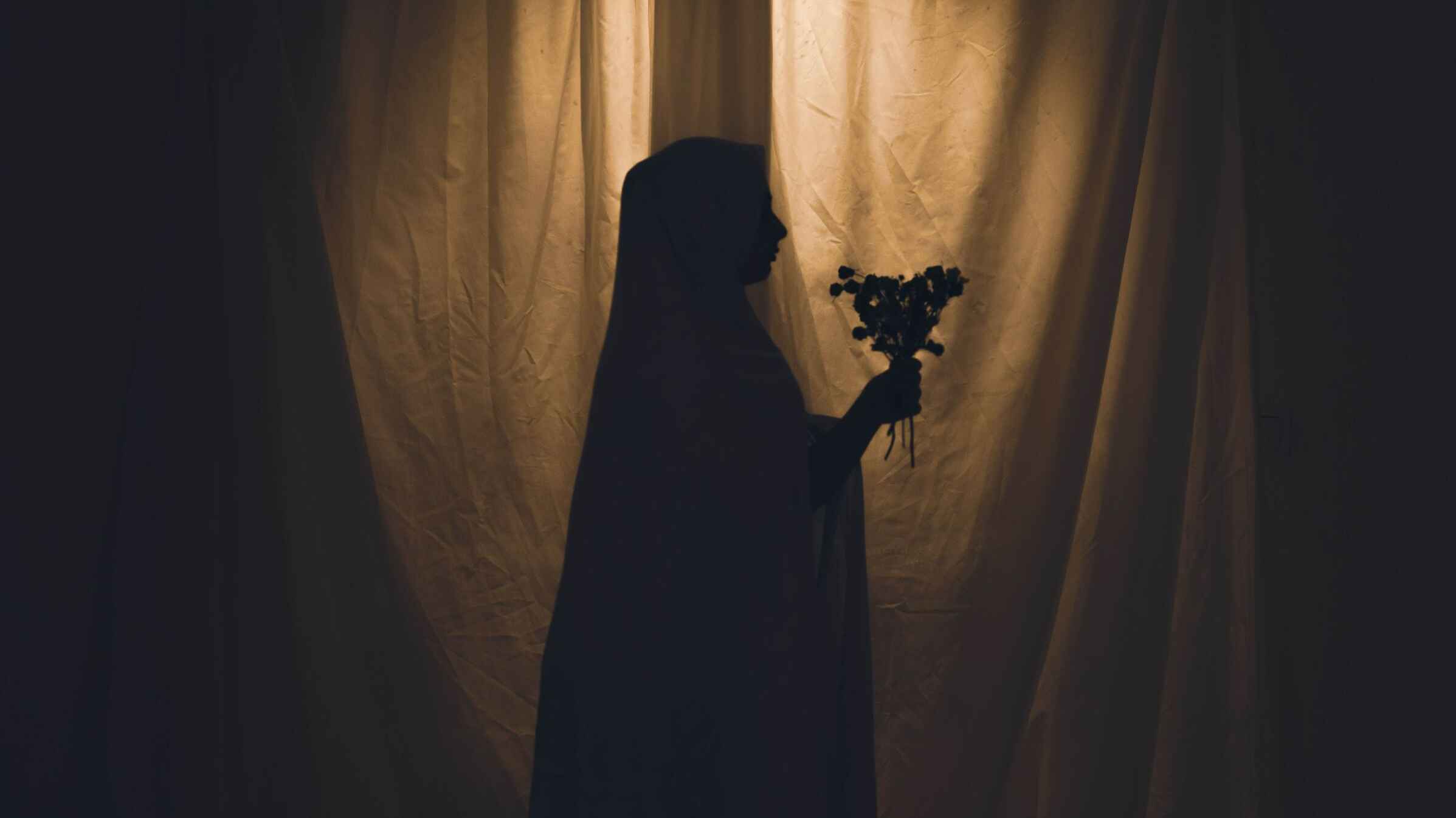 The silhouette of a young woman holding a bouquet of flowers in her hand.