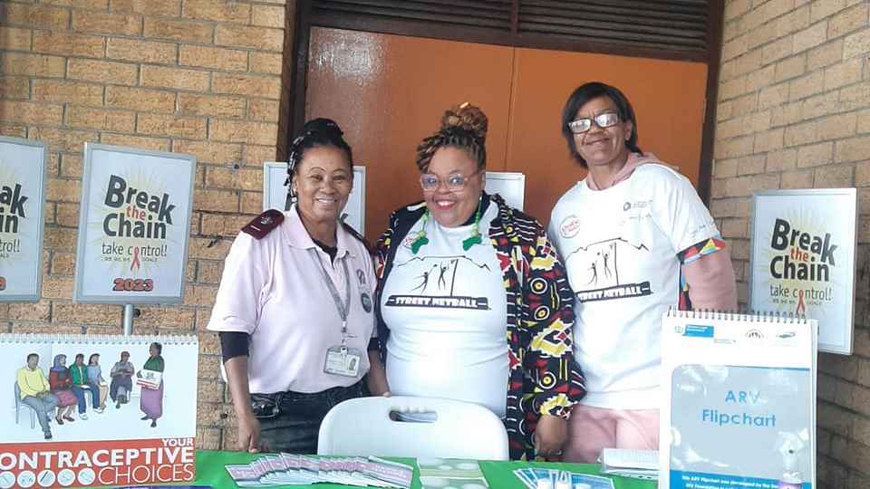 Two women and one man standing in front of a table with pamphlets and information about contraception and bodily autonomy