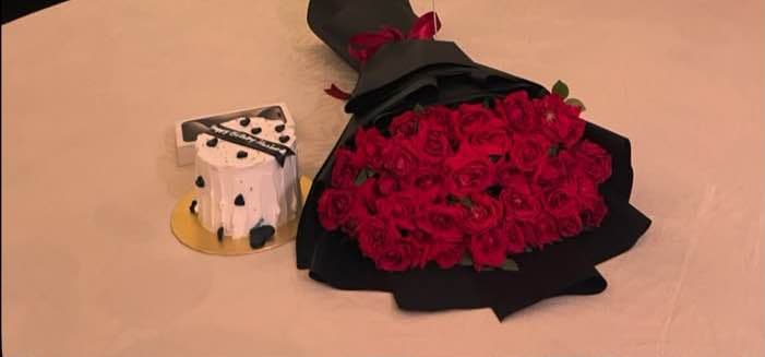 A bouquet of deep red roses wrapped in black paper, placed on a table beside a small decorative object.